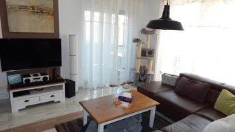 Helles Wohnzimmer mit braunem Ledersofa, Holztisch und Blick nach draußen.