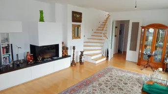 Wohnzimmer mit Kamin, hellem Holzboden und einer eleganten Holztreppe, die in die obere Etage führt.