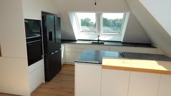 Moderne Küche im Dachgeschoss mit Kücheninsel, Einbaugeräten und Dachfenstern für viel Licht.