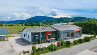 Luftaufnahme des Geschäftsgebäudes mit umliegender Landschaft und Bergen im Hintergrund unter bewölktem Himmel.