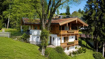 Traditionelles Alpenhaus mit Holzbalkonen und Satteldach, eingebettet in eine grüne Landschaft.