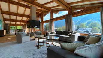 Großzügiges Wohnzimmer mit Holzbalkendecke, großen Fenstern und Bergblick.