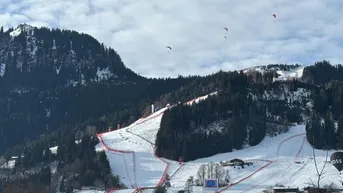 Beeindruckende Winterlandschaft mit verschneiten Skipisten und Paraglidern am Himmel.