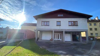 Einfamilienhaus mit Satteldach, Garagen und gepflegtem Vorgarten unter blauem Himmel.