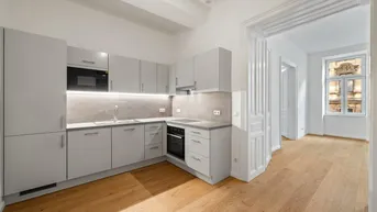 Moderne Einbauküche in Grau mit integrierten Geräten und hellem Parkettboden, offen zum Wohnbereich.