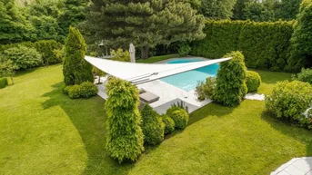 Großer Gartenbereich mit gepflegtem Rasen, einem Swimmingpool und üppiger Bepflanzung unter blauem Himmel.