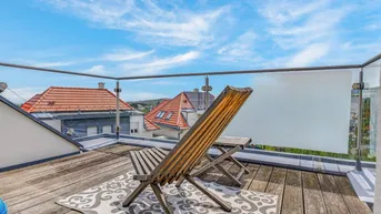 Sonniger Balkon mit Holzboden, Glasgeländer und Blick über die Dächer.