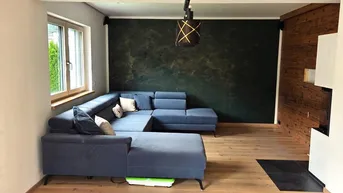 Gemütliches Wohnzimmer mit großem Ecksofa, Holzwand und dunkler Akzentwand.