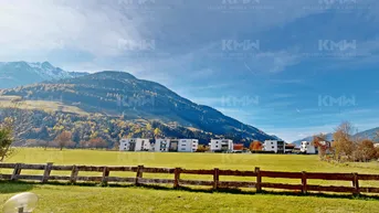 Weitläufige grüne Landschaft mit Blick auf die Berge und moderne Gebäude in der Ferne.