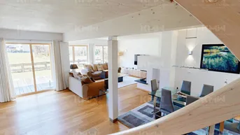 Blick von der Treppe auf den offenen Wohn- und Essbereich mit Kamin und Holzboden.