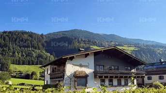 Traditionelles Haus im alpinen Stil mit Holzbalkonen und Bergblick, umgeben von grünen Hügeln und Wäldern.
