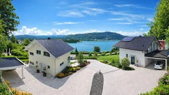 Panoramablick auf zwei moderne Häuser mit gepflasterter Auffahrt und weitem Seeblick unter blauem Himmel.