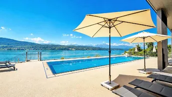Großer Außenpoolbereich mit Liegestühlen, Sonnenschirmen und weitem Blick auf den See und die Berge.