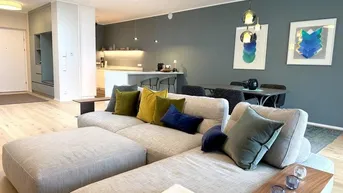 Moderner offener Wohn- und Essbereich mit bequemer Couch, Holzboden und integrierter Küche.