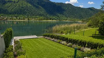 Gepflegter Gartenbereich mit direktem Seezugang und Bergblick unter blauem Himmel.