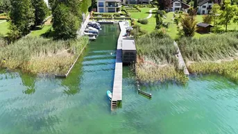 Luftaufnahme eines luxuriösen Seegrundstücks mit langem Holzsteg, modernen Häusern und üppiger grüner Umgebung.