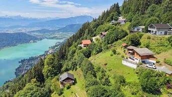 Panoramablick auf mehrere Häuser am bewaldeten Hang mit türkisfarbenem See und majestätischen Bergen im Hintergrund.