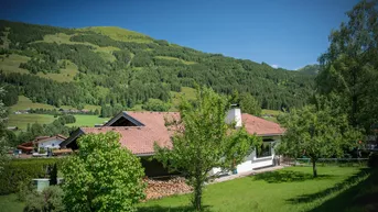 Charmantes Haus mit Ziegeldach und großem Garten, umgeben von grünen Hügeln und Wäldern.