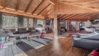 Geräumiger offener Wohnbereich mit Holzbalkendecke, großen Fenstern und gemütlicher Einrichtung.