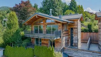 Modernes Holzchalet mit großen Fenstern und Balkonen, eingebettet in eine grüne Berglandschaft.