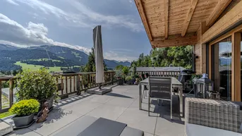 Große Terrasse mit Essbereich, Liegestühlen und beeindruckendem Bergblick unter einem Holzdach.