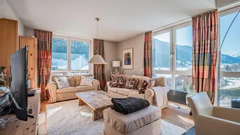 Helles Wohnzimmer mit bequemen Sofas, Holztisch und großen Fenstern mit Bergblick.