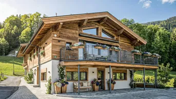 Charmantes Holzhaus im alpinen Stil mit traditioneller Architektur, Balkon und malerischem Bergblick in grüner Umgebung.