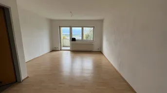 Helles, leeres Wohnzimmer mit Laminatboden und Zugang zu einem kleinen Balkon.