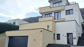 Moderne Villa mit mehreren Etagen, integrierter Garage und Außentreppe unter bewölktem Himmel.