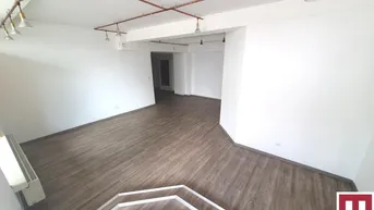Geräumiger, leerer Gewerberaum mit modernem Laminatboden und sichtbaren Deckenleitungen.
