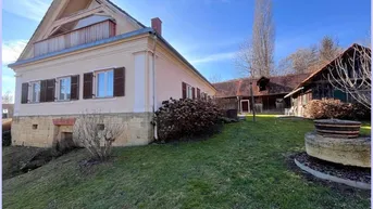 Ansicht des Haupthauses mit gepflegtem Gartenbereich und einem traditionellen Steinelement unter blauem Himmel.
