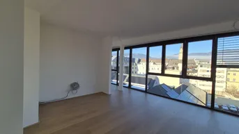Heller, leerer Wohnraum mit großen Fenstern und weitem Blick auf die Stadt und Berge.