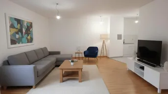 Helles Wohnzimmer mit modernem Sofa, Holztisch und offener Küchenzeile im Hintergrund.