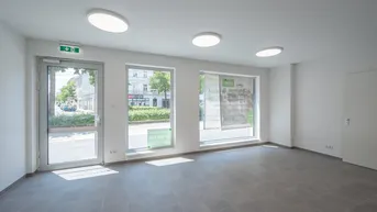 Heller, moderner Gewerberaum mit großen Fenstern zur Straße und grauem Fliesenboden.