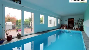 Heller Innenpoolbereich mit großen Fenstern, die den Blick auf die Terrasse und den Garten freigeben.