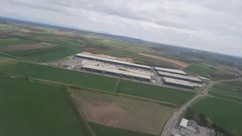 Luftaufnahme einer Industrieanlage umgeben von weiten Feldern unter bewölktem Himmel.