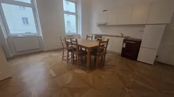 Helle Küche mit weißen Schränken, Esstisch und Parkettboden, ideal für gemeinsame Mahlzeiten.