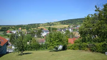 Weitläufiger Blick über die grüne Landschaft mit verstreuten Häusern und Hügeln.