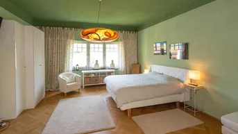 Geräumiges Schlafzimmer mit grünen Wänden, Parkettboden und einem großen Fenster, das viel Licht hereinlässt.