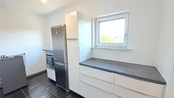 Funktionale Küche mit weißen Schränken, dunkler Arbeitsplatte und Fenster mit Ausblick.