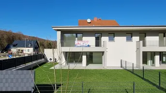 Modernes Doppelhaus mit großem Garten und Balkonen, umgeben von grüner Landschaft.