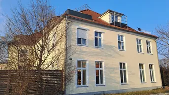 Modernes Mehrfamilienhaus mit heller Fassade, Satteldach und Rollläden in sonniger Lage.