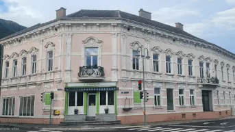 Historisches Eckgebäude mit Stuckfassade und kleinem Balkon in bergiger Umgebung.