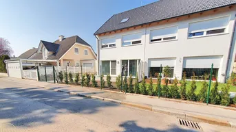 Modernes Reihenhaus mit weißer Fassade, Rollläden und kleinem Vorgarten an einer ruhigen Straße.
