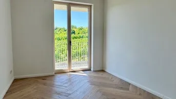 Leeres Zimmer mit Fischgrätparkett und Zugang zu einem französischen Balkon mit Weinbergblick.
