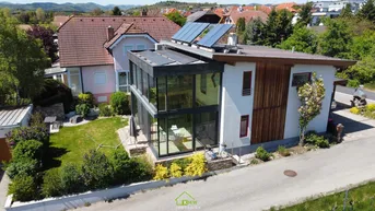 Drohnenaufnahme eines modernen Hauses mit Glasanbau, Solarpaneelen auf dem Dach und einem gepflegten Garten.