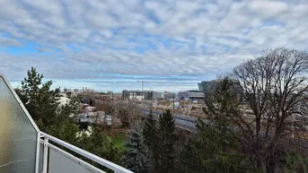 Weitblick vom Balkon über die Stadt mit Bäumen und Bahngleisen unter einem bewölkten Himmel.