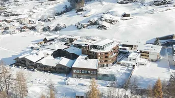 Winterliche Luftaufnahme des Hotelkomplexes eingebettet in eine verschneite Alpenlandschaft.