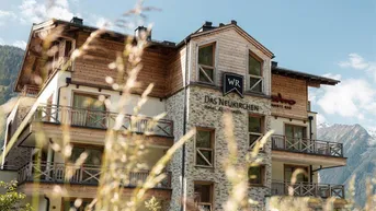 Modernes Gebäude mit Holzfassade und Balkonen in alpiner Umgebung.