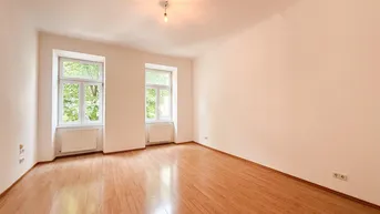 Helles, leeres Zimmer mit Parkettboden und zwei Fenstern, die viel Tageslicht hereinlassen.